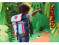 Child with blue and red backpack, pointing in a paper jungle setting.
