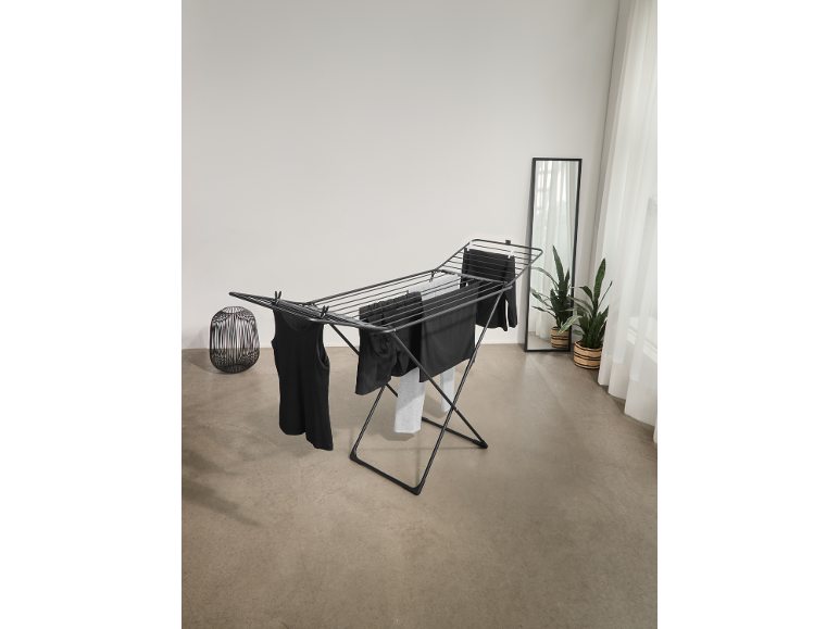 Black clothes drying rack with dark laundry in a bright room.