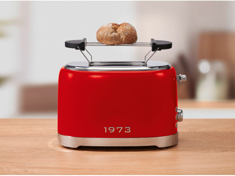 Red toaster with a bread roll on the warming rack, on a wooden table.