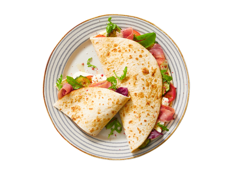 Piadina with ham, mozzarella, tomato, zucchini, and arugula on a striped plate.