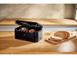 Black bread bin with bread and sliced wholemeal bread on a wooden table.