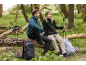 Two hikers in sports jackets and trousers, sitting on a tree trunk with backpacks and walking poles.