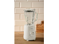 White stand mixer with glass jug and wooden base, on a kitchen counter with light tiles.