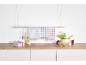 Red checkered kitchen towels hanging and stacked on a wooden counter with utensils and plants.