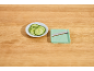 Sliced cucumbers on a plate next to a mint green mandoline on a wooden table.