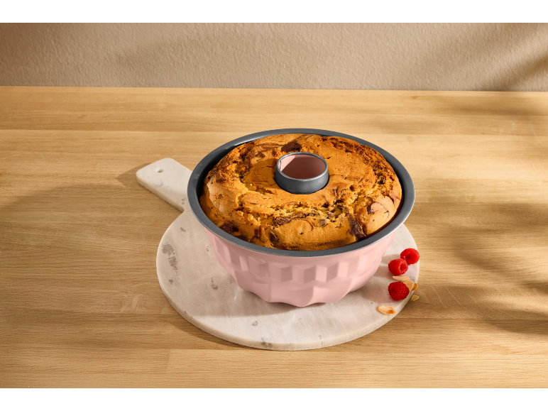 Cake in a pink bundt pan on a marble board, garnished with raspberries.