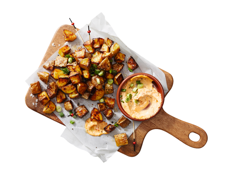 Roasted potatoes with spring onions and creamy sauce on a wooden board.