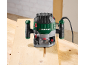 Green and black electric router on a wooden table with a groove.