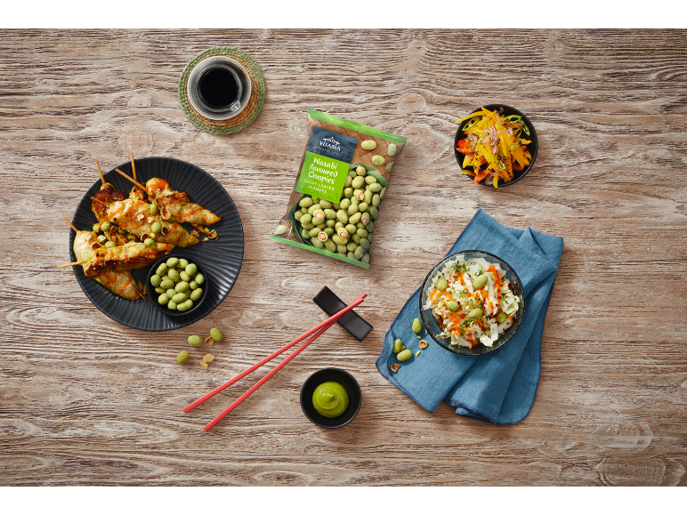 Asian food with chicken skewers, salads, and wasabi peanuts on a wooden table.