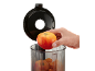 A hand places an apple into a clear container with other apples, with a black lid in the background.