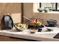 Glass bowls with black lids filled with salad and roasted vegetables on a kitchen counter.