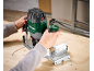 A person uses an electric router to cut wood, creating a curved groove.