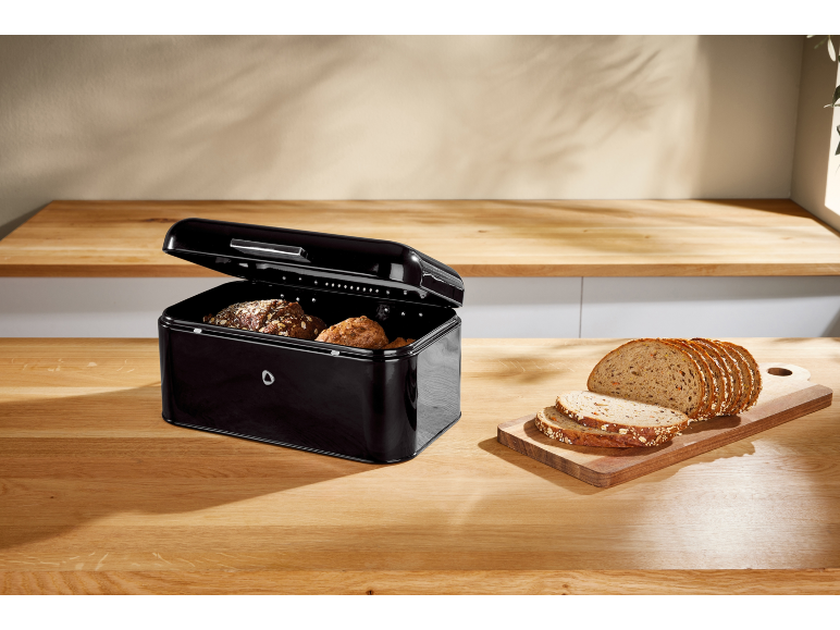 Black bread bin with bread and sliced wholemeal bread on a wooden countertop.
