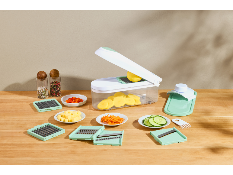 Vegetable chopper with various blades, sliced potatoes, carrots, cucumbers, and peppers.