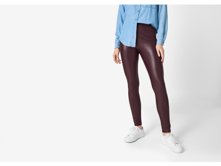 Woman in blue denim shirt and burgundy faux leather leggings, with white sneakers.