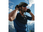 Man in a cycling helmet, sunglasses, and gloves against a mountainous backdrop.