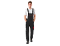 Man in black work overalls and white t-shirt, with hands in pockets, smiling.