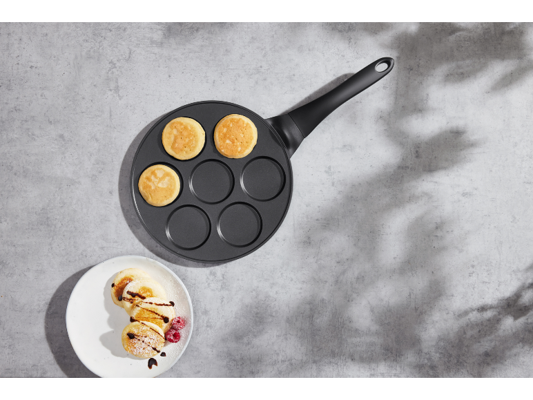 Pancake pan with pancakes and a plate of pancakes with fruit and chocolate.