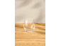Clear stemless glass on a light wooden table with subtle wall shadows.