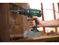 Green cordless drill drilling into wood, with wood chips flying.
