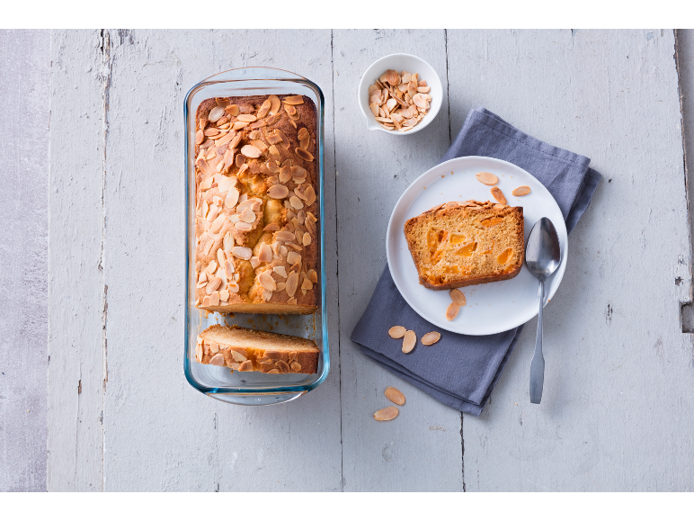Almond and apricot loaf cake in a glass pan, with a slice on a plate