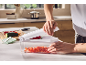 Person using a vegetable chopper to dice red bell peppers in a bright kitchen.