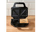 Open sandwich maker with one toasted sandwich on a wooden table.