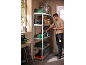 Man in workwear organizing tools on metal shelves in a workshop.