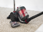 Red and grey bagless vacuum cleaner on light carpet with attachment