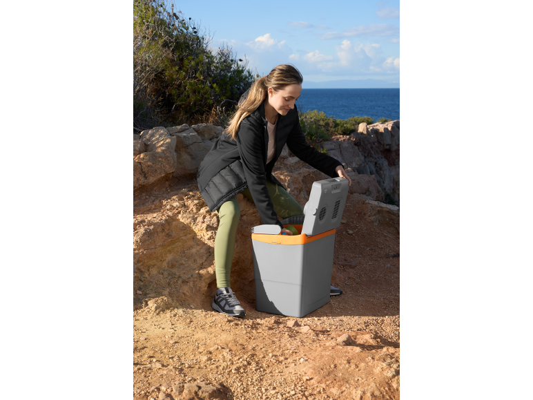 Woman opening a portable electric cool box on a rocky coastal path