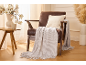 Brown armchair with a beige cushion and blanket, next to a table with a magnolia vase.
