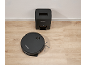Black robot vacuum cleaner and auto-empty station on a wooden floor.