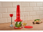 Red immersion blender with chopper and measuring cup on a wooden surface.