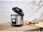 Rice cooker with cooked rice, a bowl of rice, and a spoon on a wooden counter.