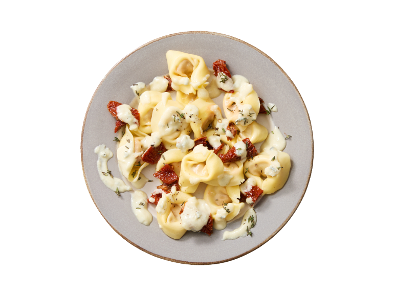 Tortellini with cheese sauce, sun-dried tomatoes, and herbs on a plate.