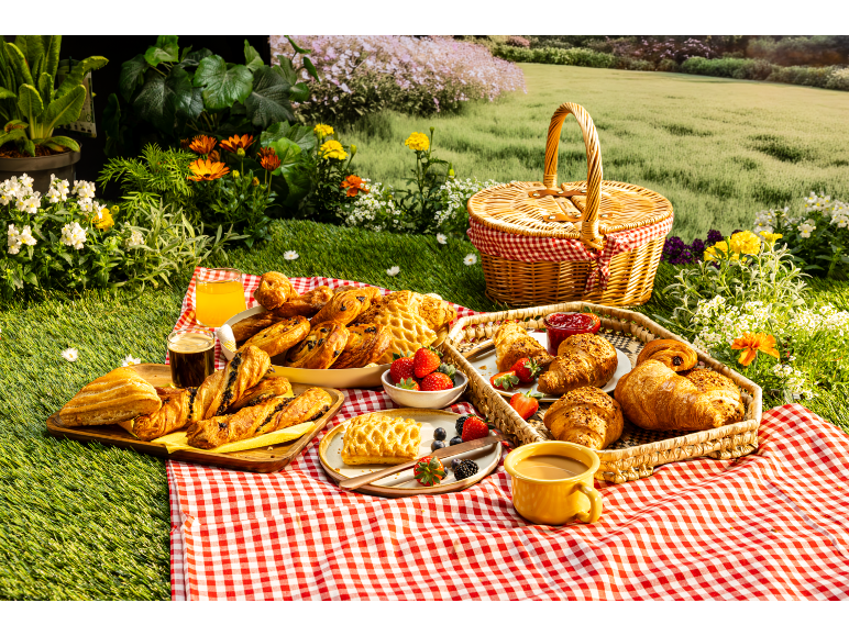 Picnic with a variety of pastries, berries, and drinks on a red checkered blanket.