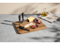 Cheese board with cheeses, grapes, and figs, accompanied by cheese knives and an oil bottle.