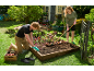 Man and woman planting in a raised garden bed, surrounded by tools and plants.