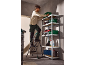 Man on a step ladder placing a green toolbox onto a metal shelving unit.