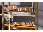 Copper pots and pans on wooden shelves, next to jars with grains.