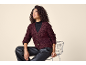 Woman in a burgundy knitted cardigan and black faux leather trousers, sitting on a chair.