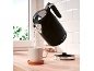 Black kettle with the number 1973 pouring water into a mug on a wooden counter.