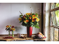 Autumnal floral arrangement with yellow, orange, and red flowers, fruits, and vegetables.