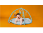 Baby crawling on a playmat with arches and hanging toys on an orange background.