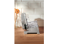 Gray electric food slicer on a wooden countertop with kitchen utensils in the background.