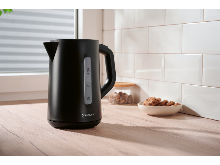 Black electric kettle on a wooden countertop with white tiles and cookies.