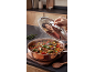 Steaming vegetable stew in a copper pot, with a person's reflection in the lid.