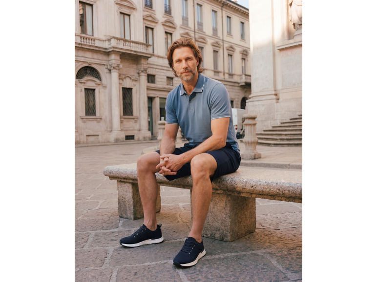 Man in blue polo shirt and dark shorts sitting on a stone bench.