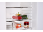 Fridge interior with a clear organizer full of vegetables and a jar of jam.