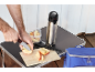 Man cutting apples with a knife on a camping table with a thermal bottle.